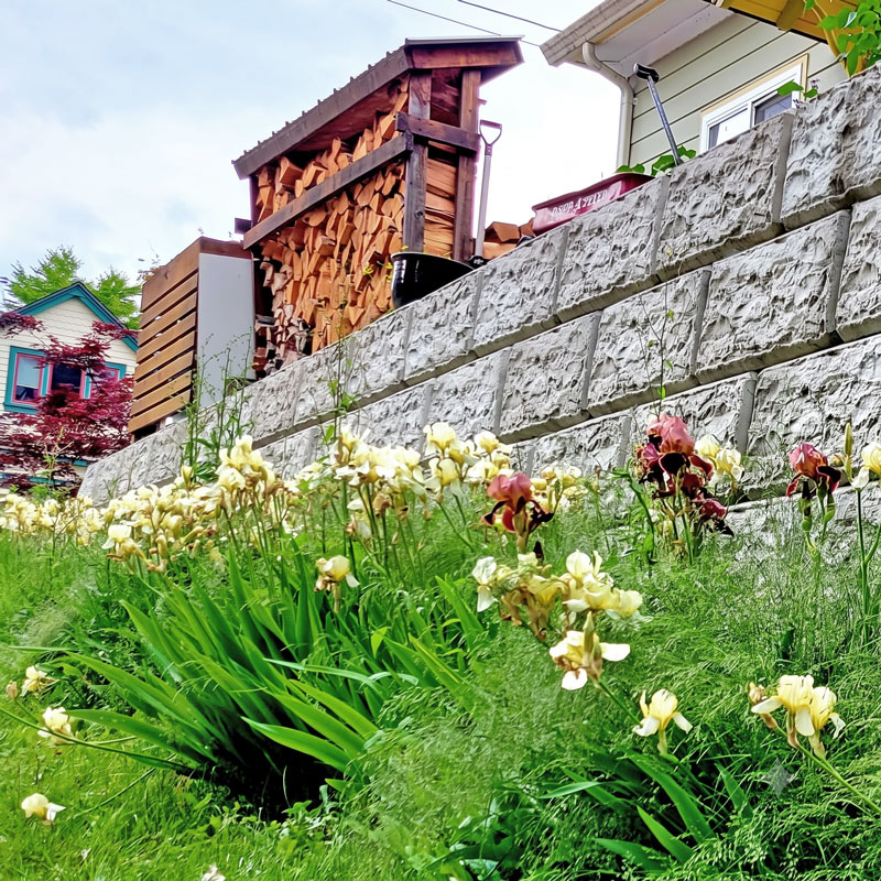 Tiered architectural concrete block retaining walls paired with residential landscaping and floral garden beds.